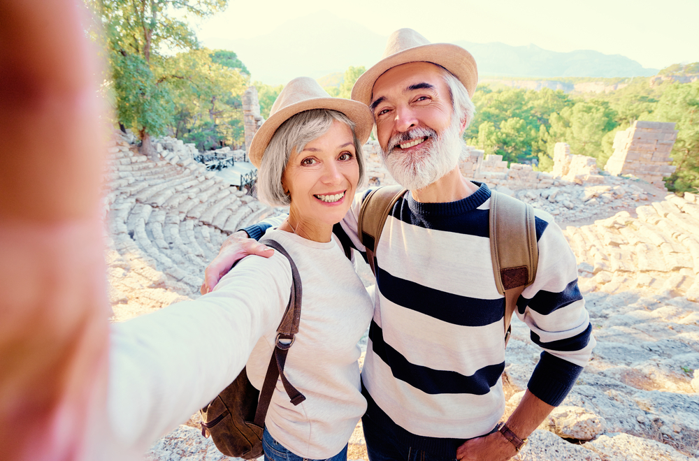 Tourism and technology. Traveling senior couple taking selfie together against ancient sightseeing background.